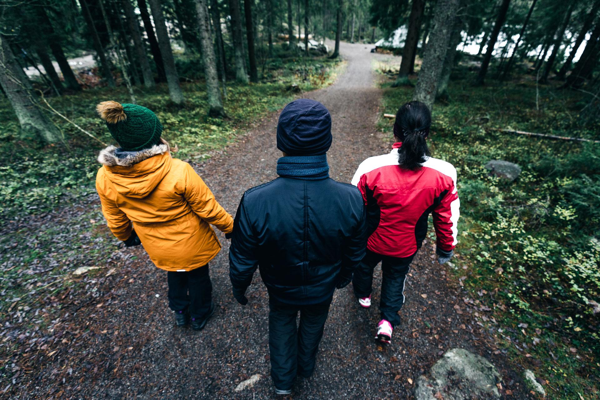 Kuvassa kolme henkilöä kävelee metsätiellä selin kameraan.