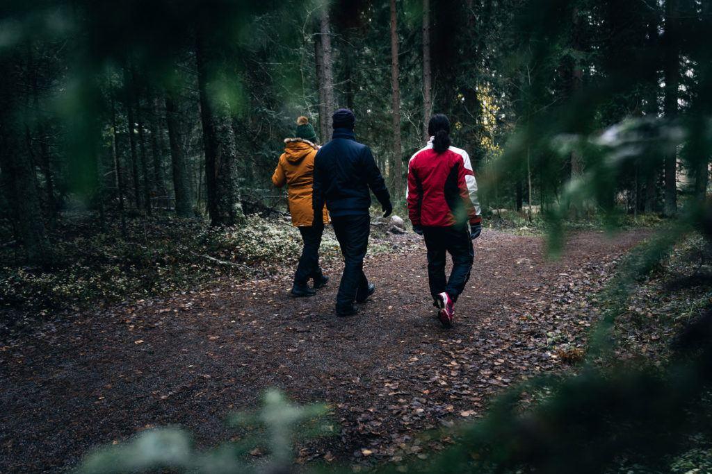 Kolme henkilöä kävelee metsätiellä selkä kameraan päin.