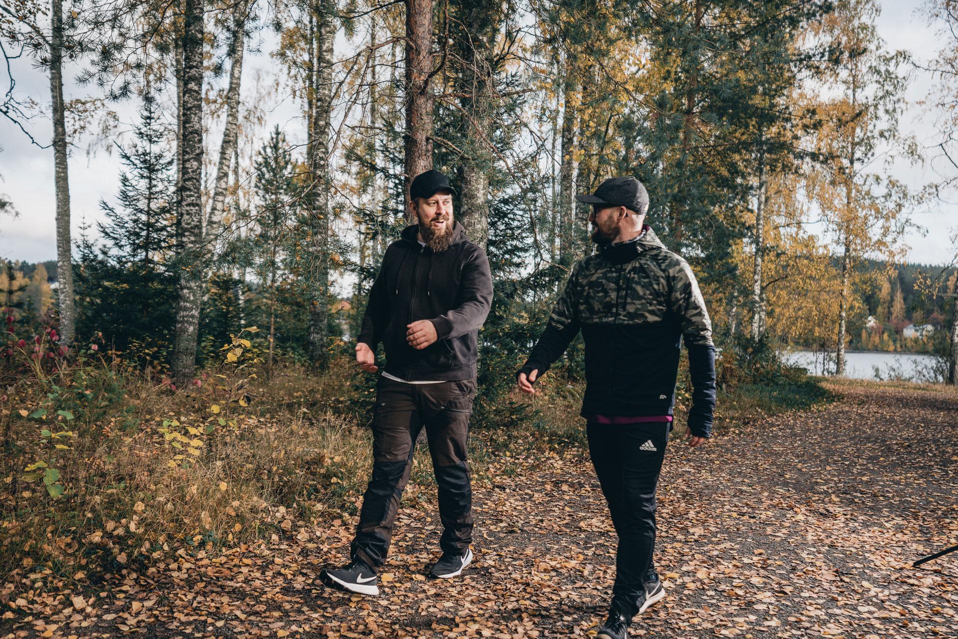 Kaksi miestä kävelee syksyisessä metsässä.