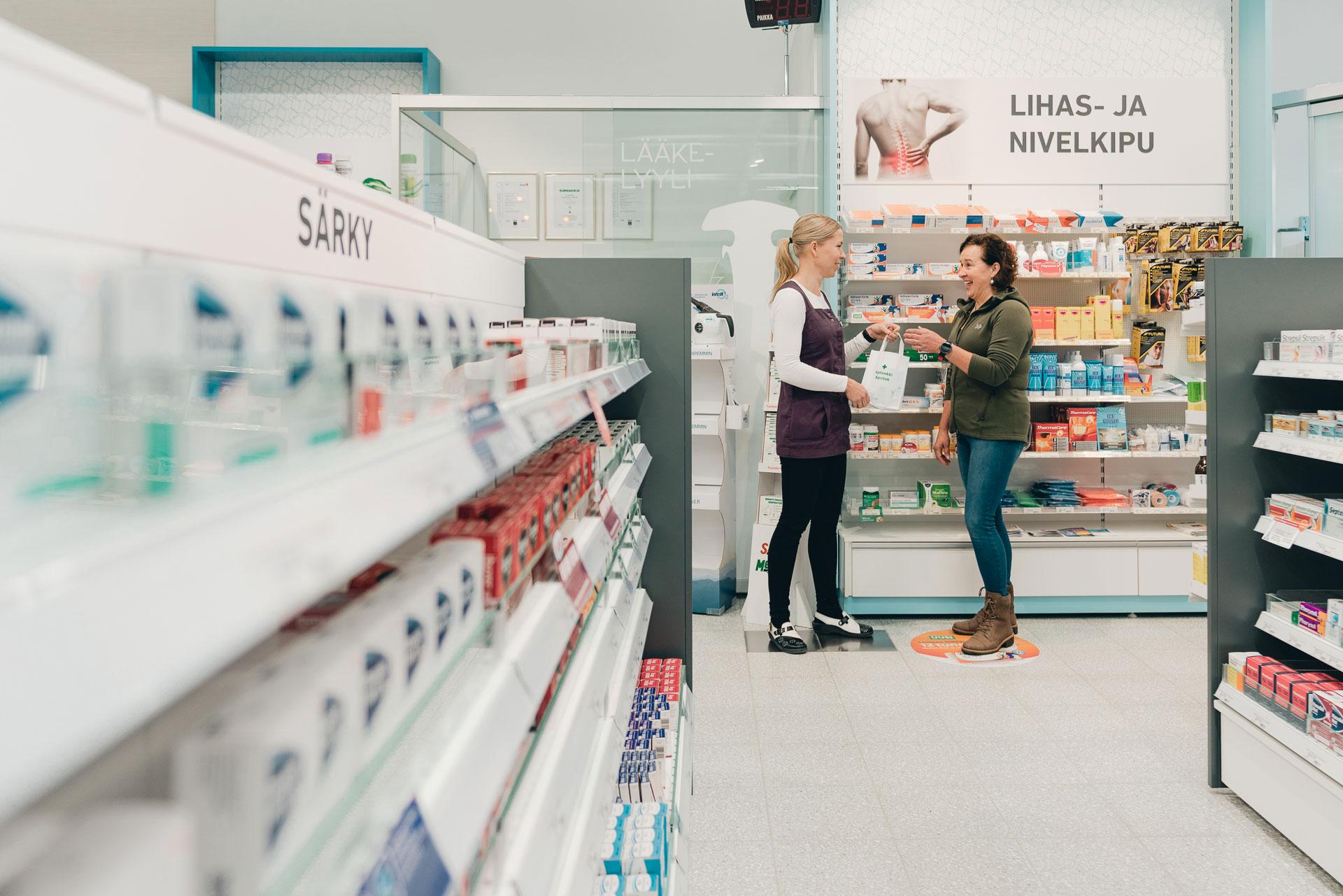 The pharmacist hands the customer a paper bag at the pharmacy shelf.