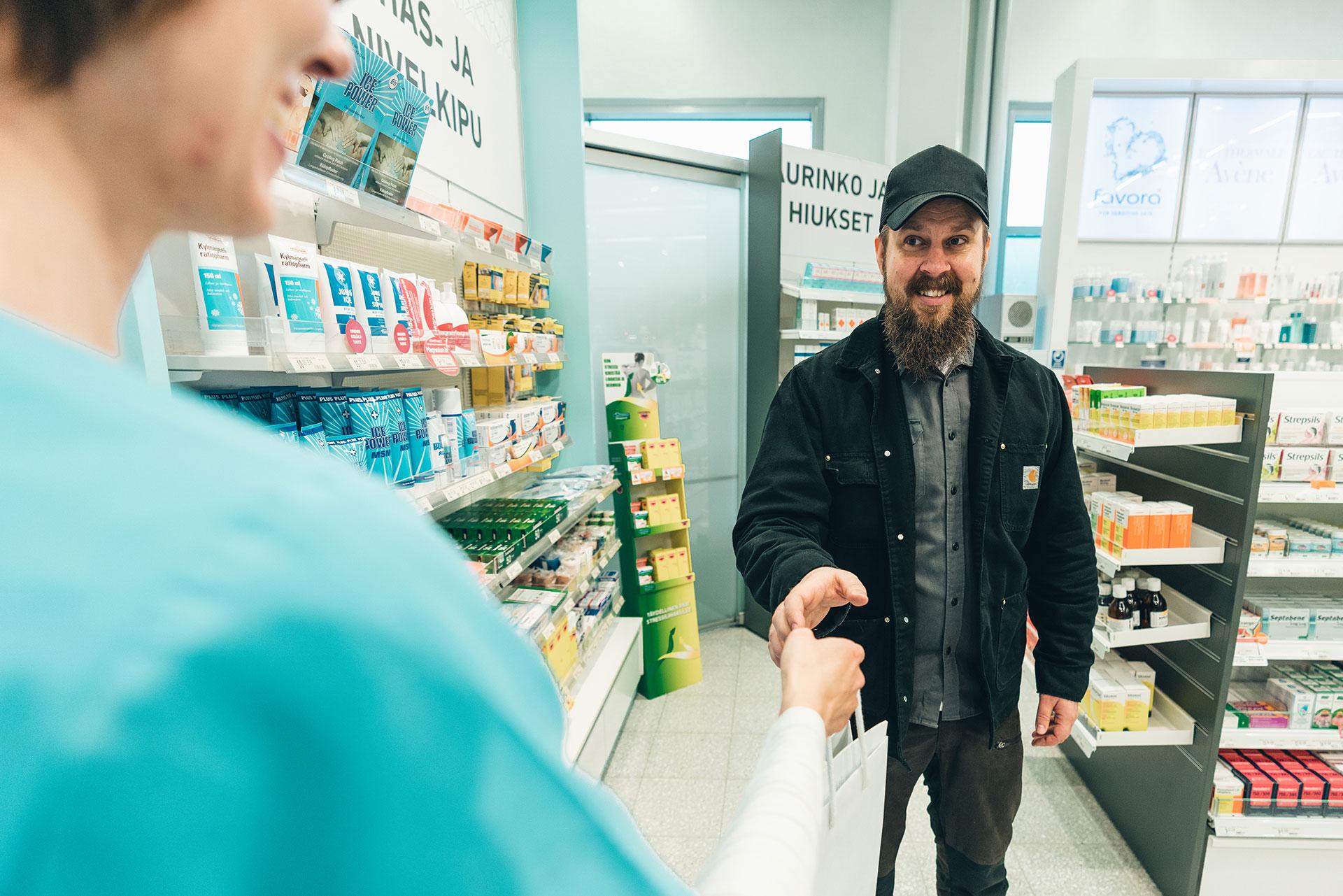 A woman hands a man a paper bag at a pharmacy.